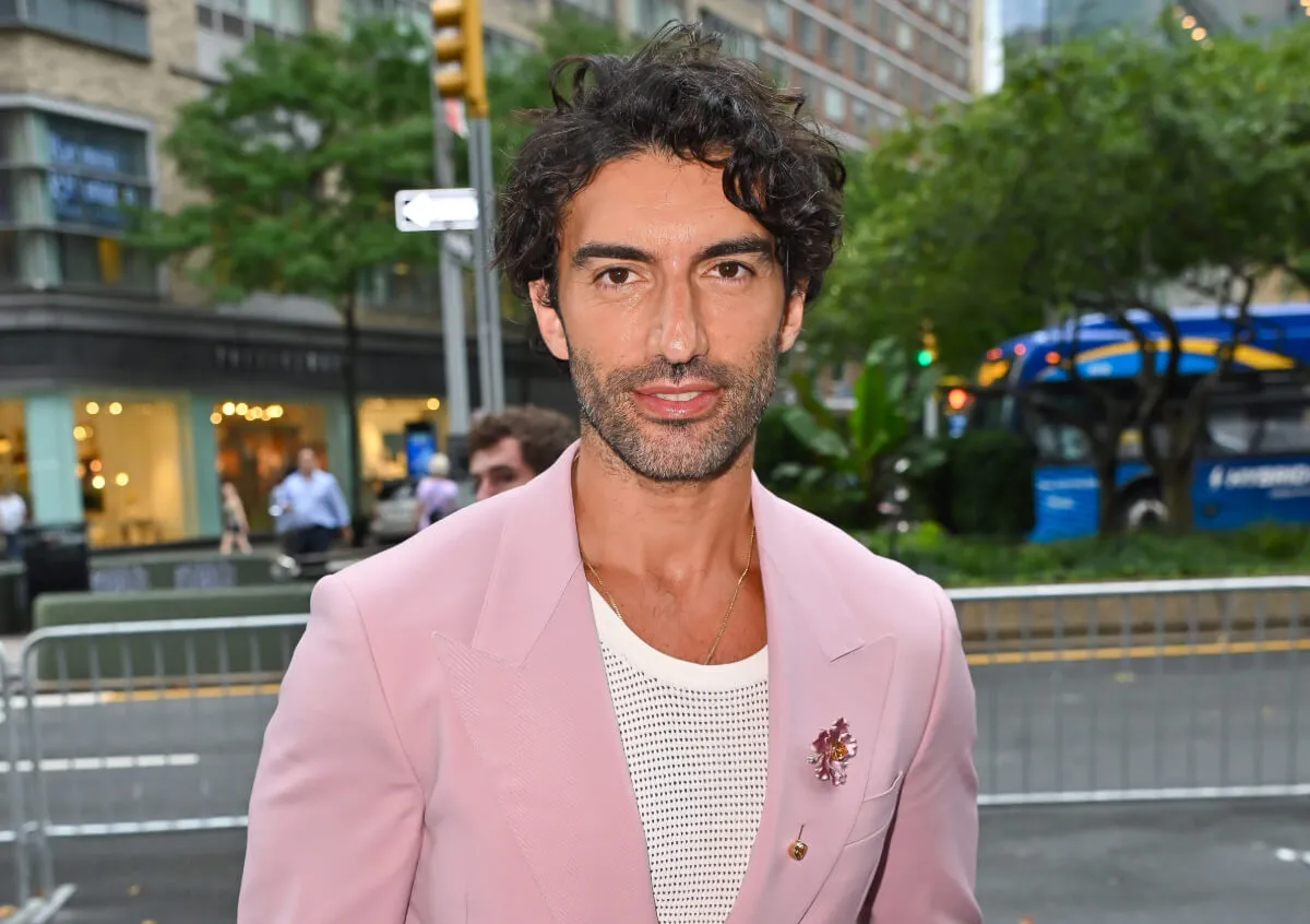 Justin Baldoni wears a pink suit and stands outside.