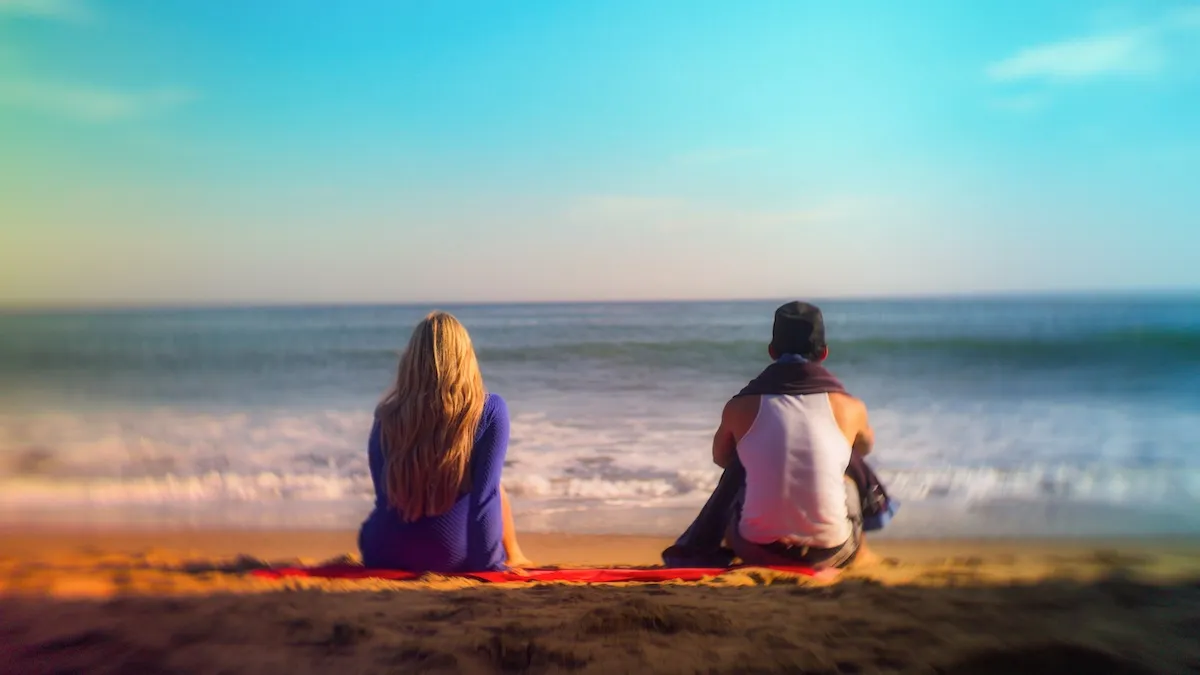 Two people sitting on a beach with their backs to the camera in 'Calabasas Confidential'