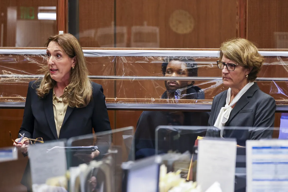 Image of D4vd behind plexiglass in court with his two female lawyers standing in front of glass