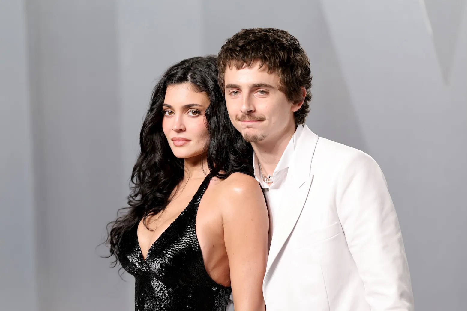 Kylie Jenner and Timothée Chalamet posing at the 2026 Vanity Fair Oscar Party. She's in a black dress and he's in a white suit.