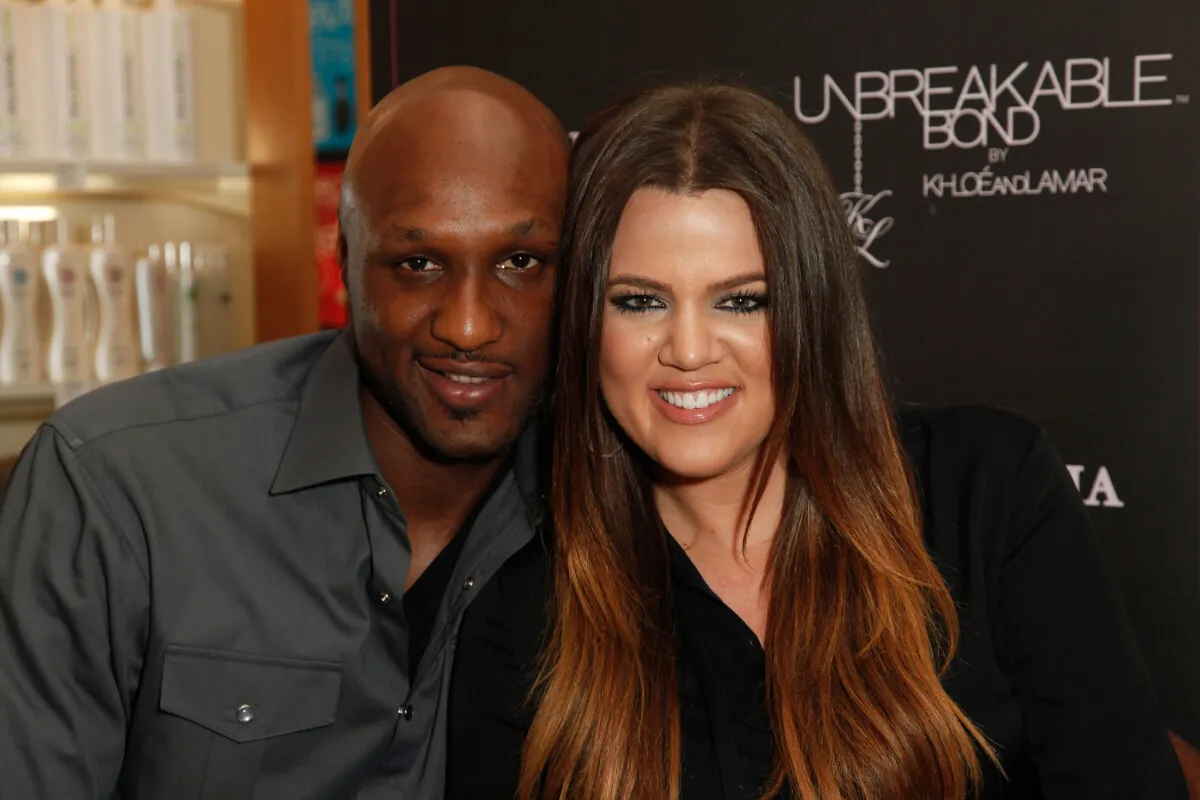 Lamar Odom wears a gray shirt and smiles next to Khloe Kardashian. She wears black.