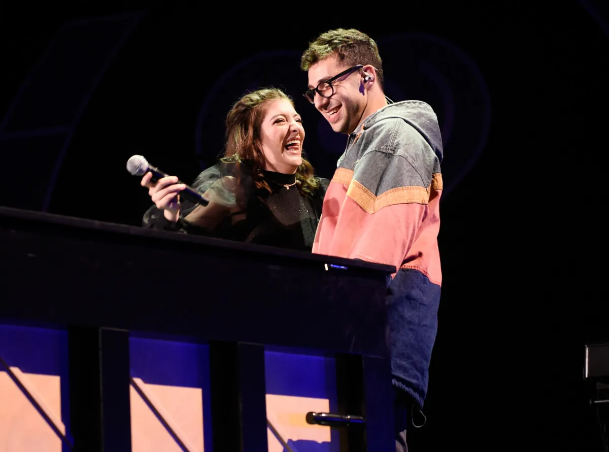 Lorde wears black and holds a microphone. She stands with Jack Antonoff, who wears a sweatshirt and glasses.