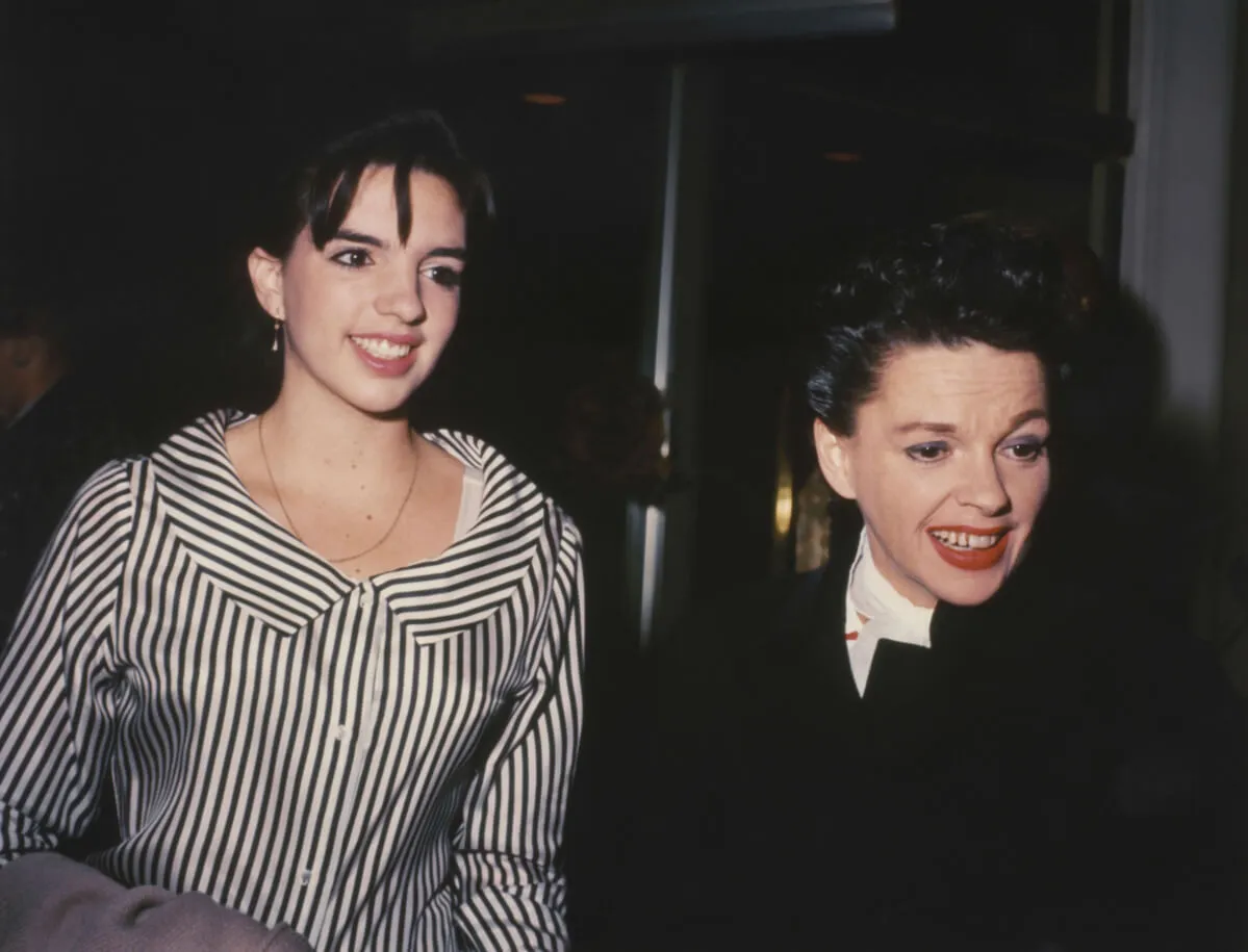 Liza Minnelli wears a black and white striped shirt and walks with Judy Garland, who wears black.