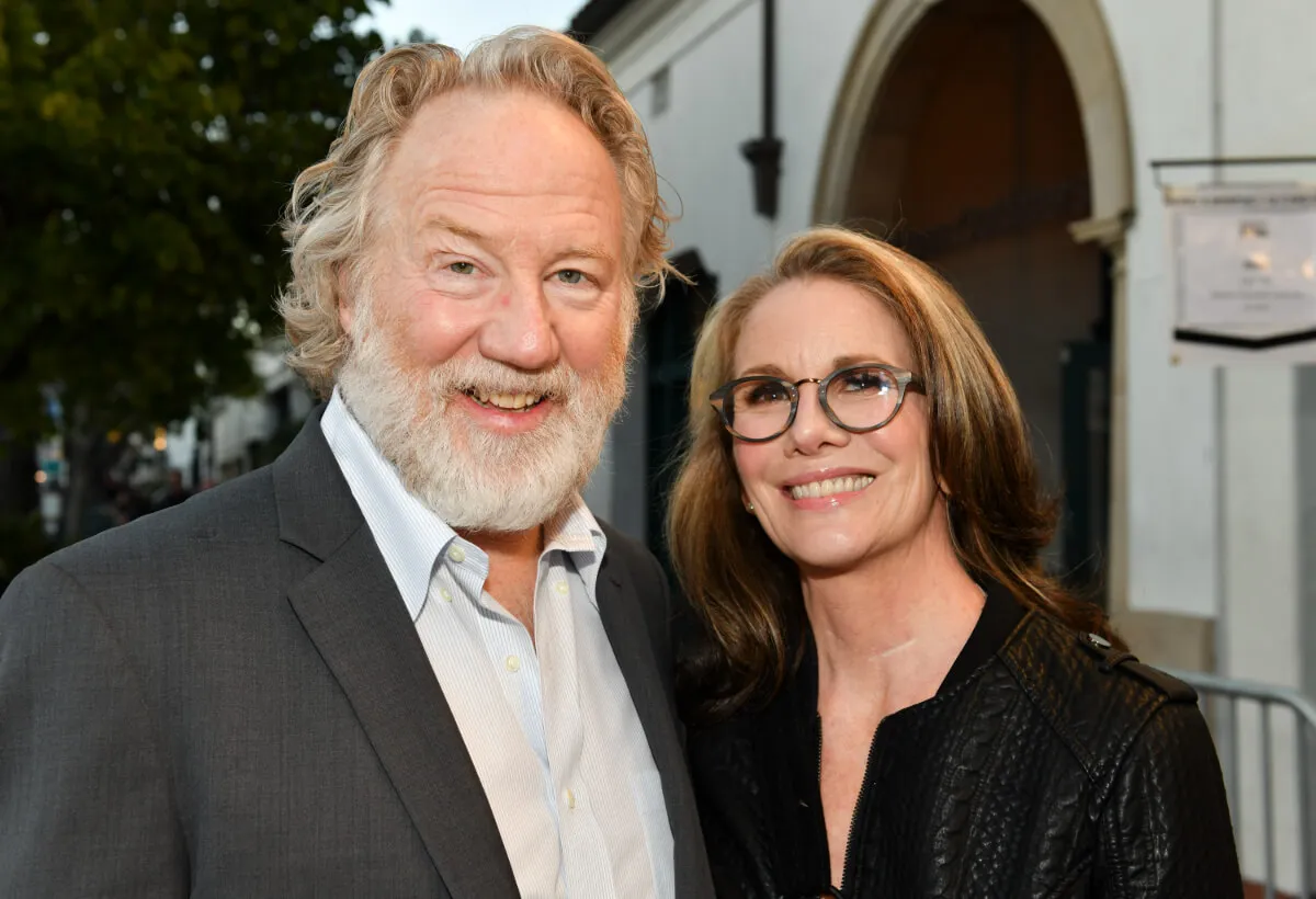 Timothy Busfield wears a suit and stands with Melissa Gilbert, who wears glasses and a black shirt.