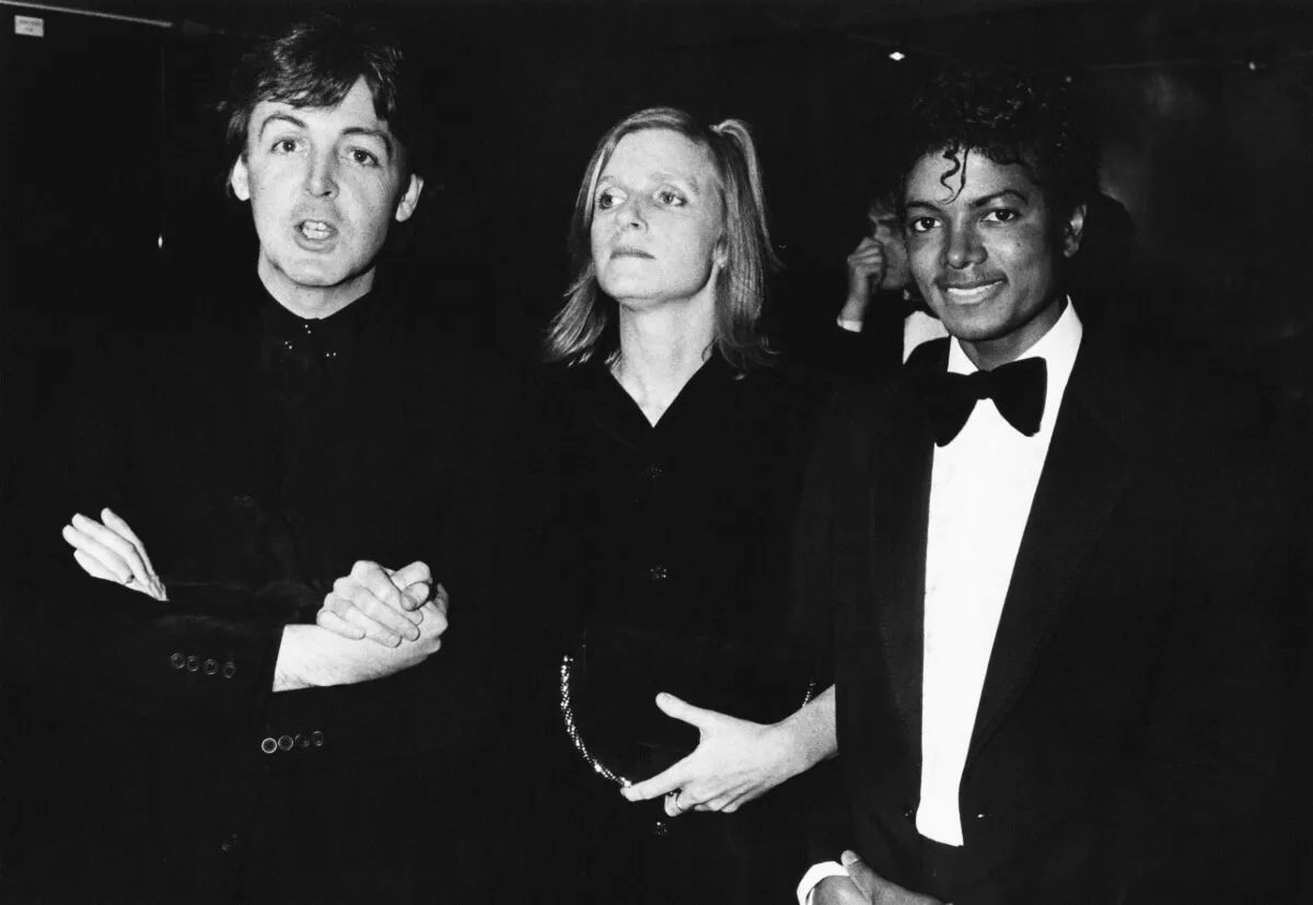 A black and white picture of Paul and Linda McCartney standing with Michael Jackson. Jackson wears a tuxedo and the McCartneys wear black.