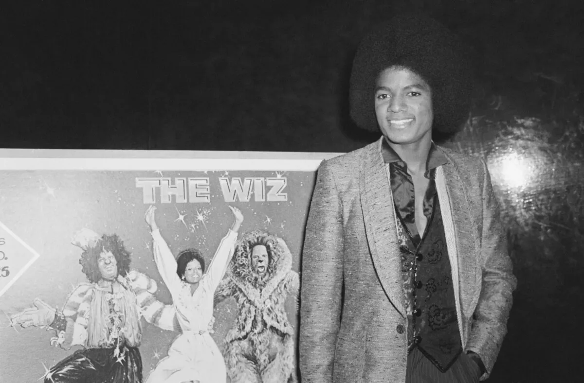 A black and white picture of Michael Jackson standing in front of a sign for 'The Wiz.'