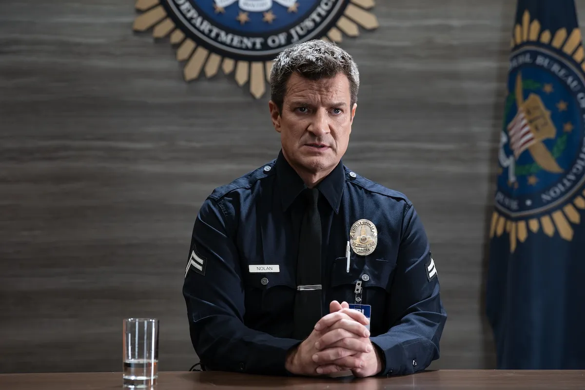 Nathan Fillion sitting at a table and wearing an LAPD uniform in 'The Rookie' Season 8
