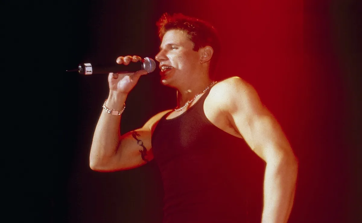 NIck Lachey, wearing a black tank top, singing into a microphone while performing with 98 Degrees