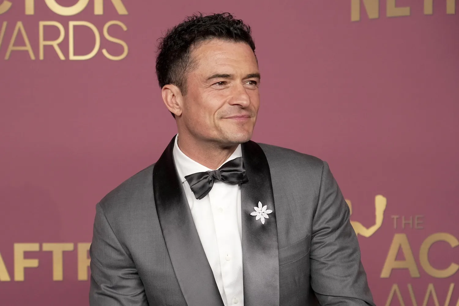 Orlando Bloom in a tuxedo against a pink background at the Actor Awards in 2026