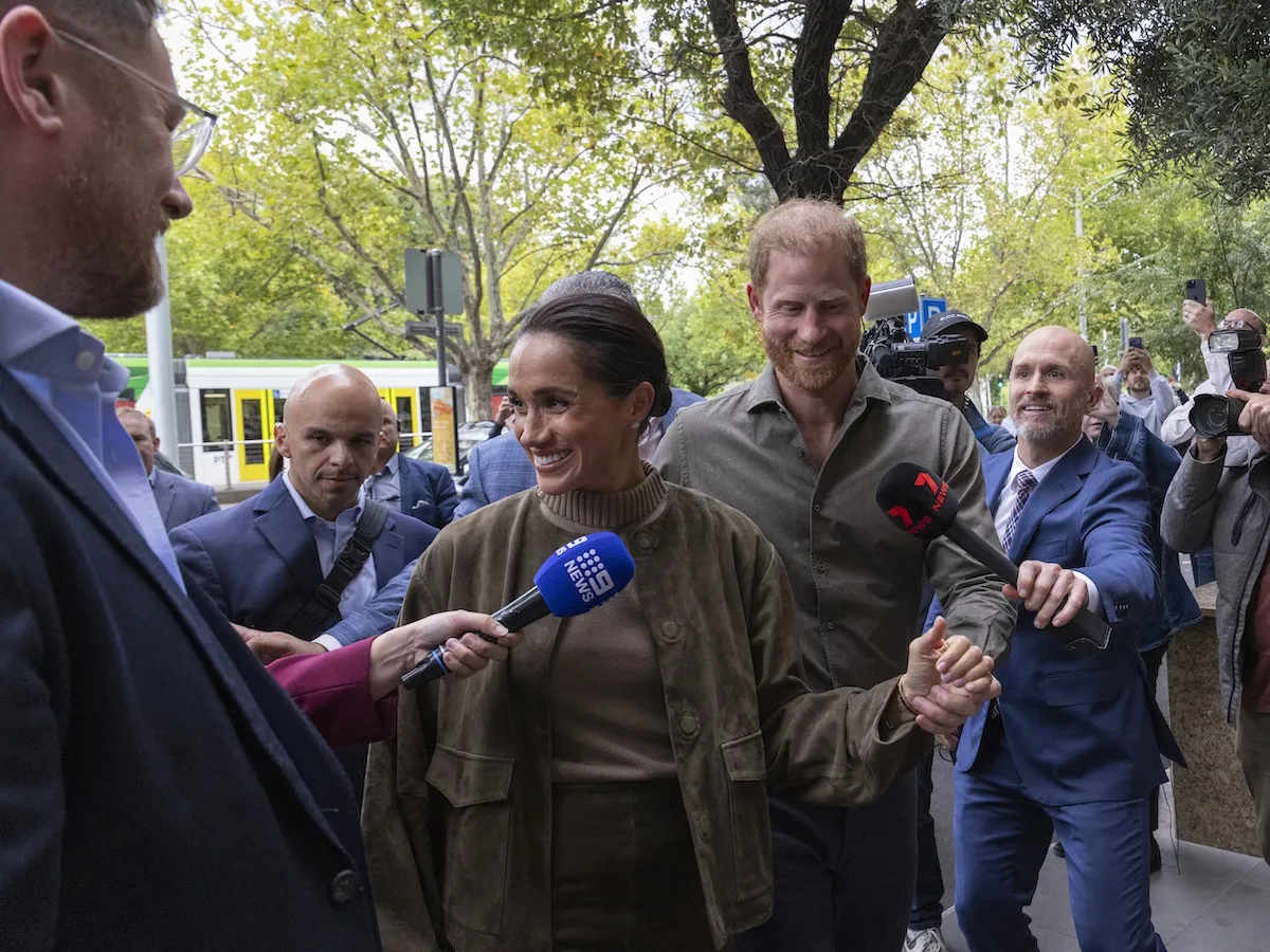 Meghan Markle and Prince Harry in front of reporters holding microphones
