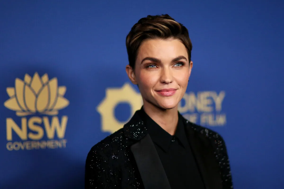 Ruby Rose wears a black sequined blazer and stands in front of a blue background.