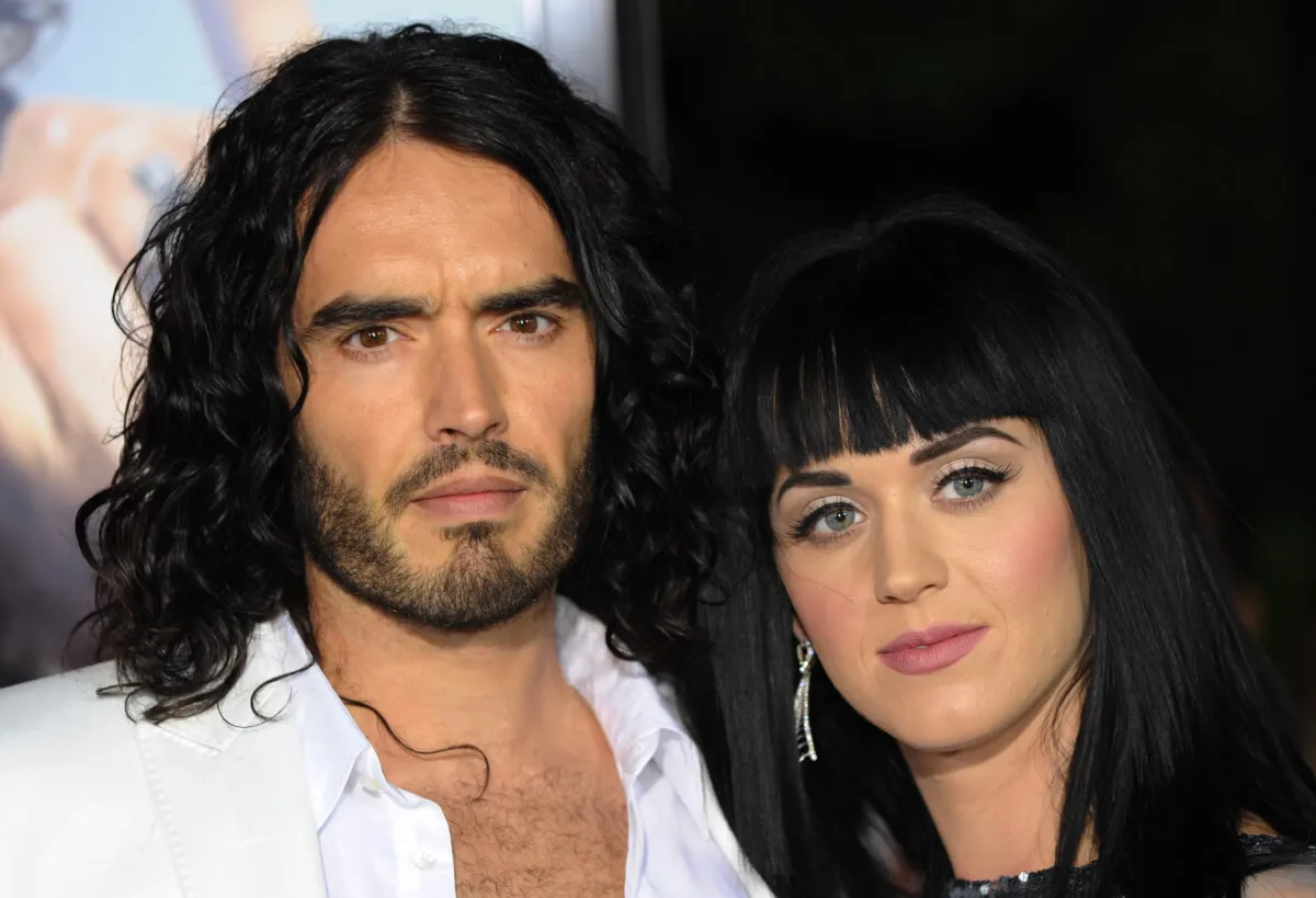Russell Brand wears a white shirt and stands with Katy Perry.