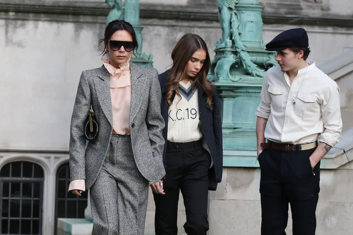 Victoria Beckham, in a suit, walking front of Hana Cross and Brooklyn Beckham