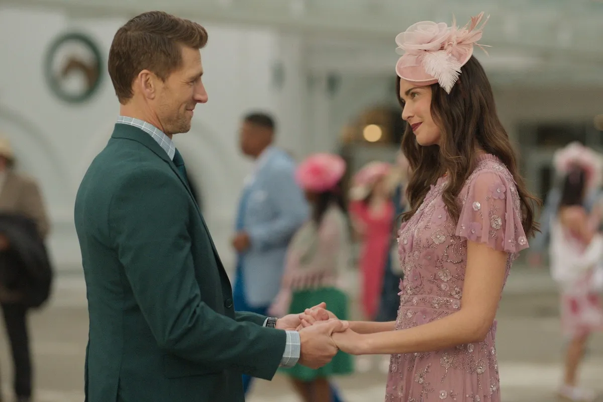 Man in a suit holding hands with a woman in a hat