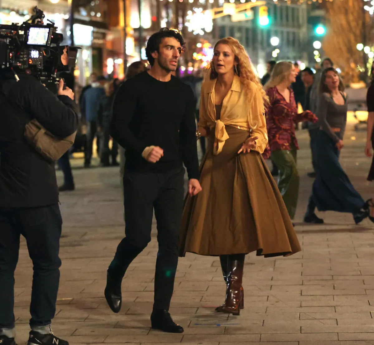 Justin Baldoni wears black and stands with Blake Lively while filming 'It Ends With Us.' She wears a brown skirt.