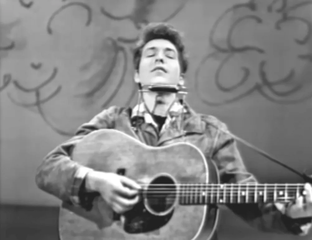 A black and white screen shot of Bob Dylan playing guitar on television in 1963.