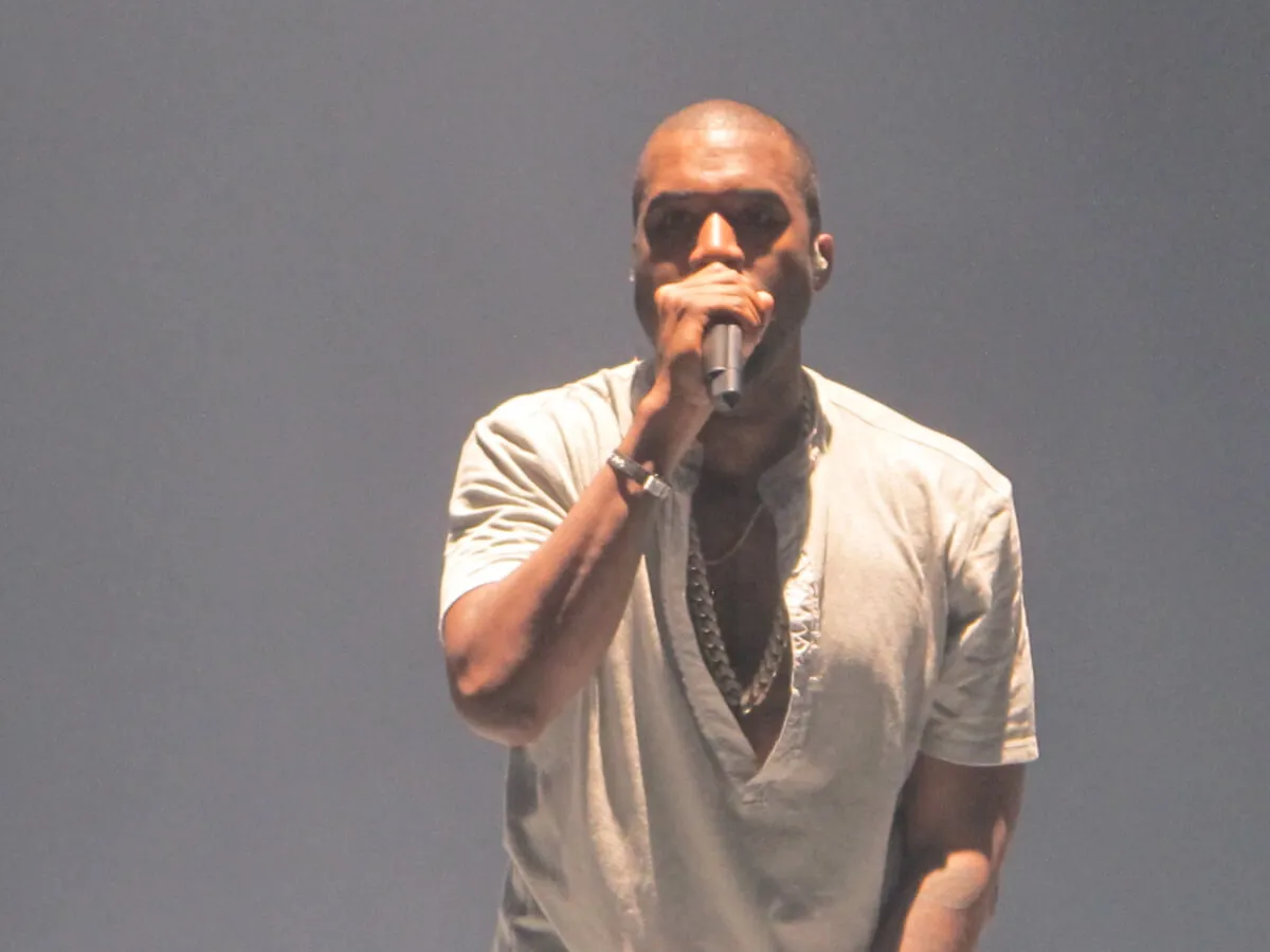 Kanye West wears a white shirt and holds a microphone.