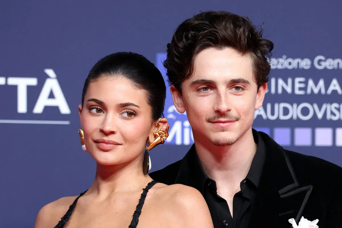 Kylie Jenner wears large gold earrings and stands with Timothee Chalamet. They both wear black.