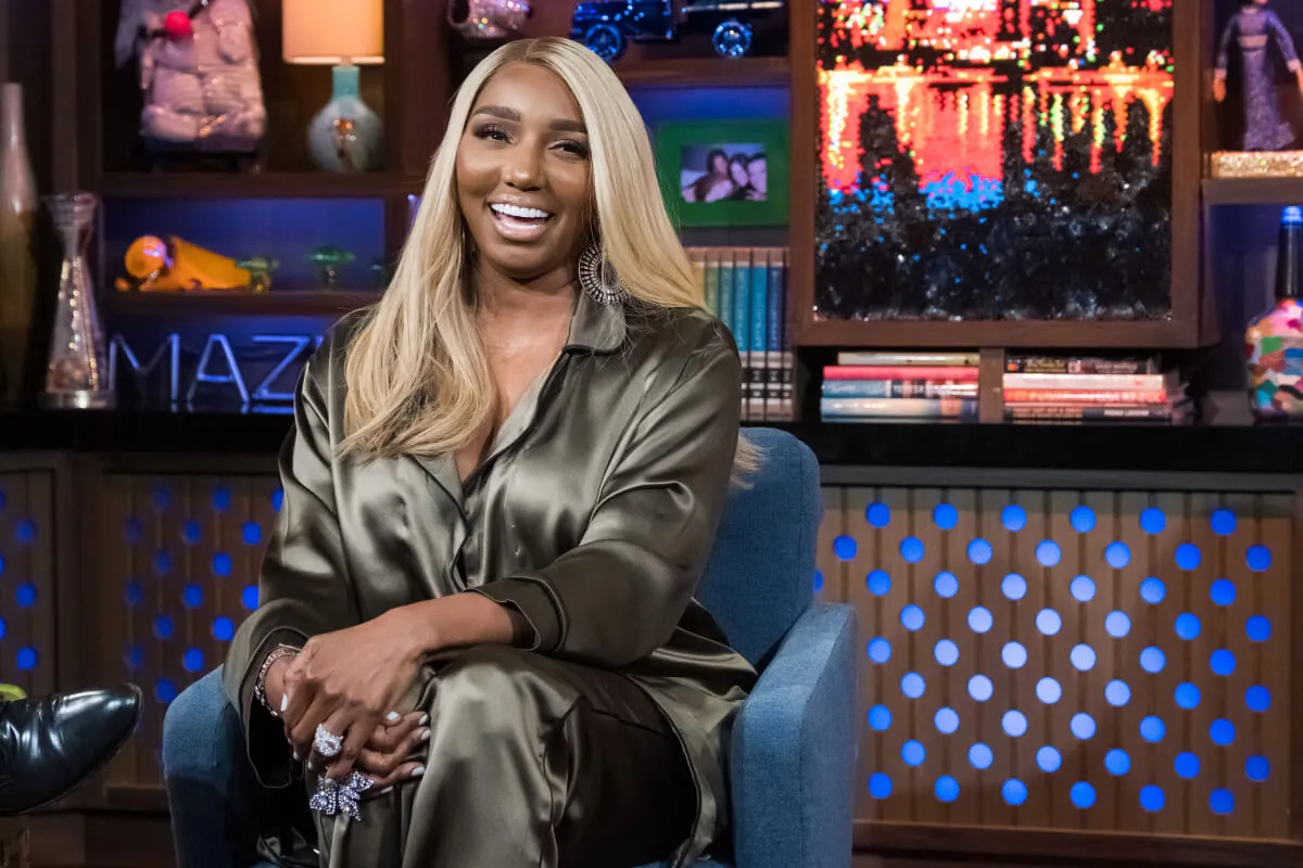 NeNe Leakes wears a brown silk jumpsuit and sits in a blue armchair.