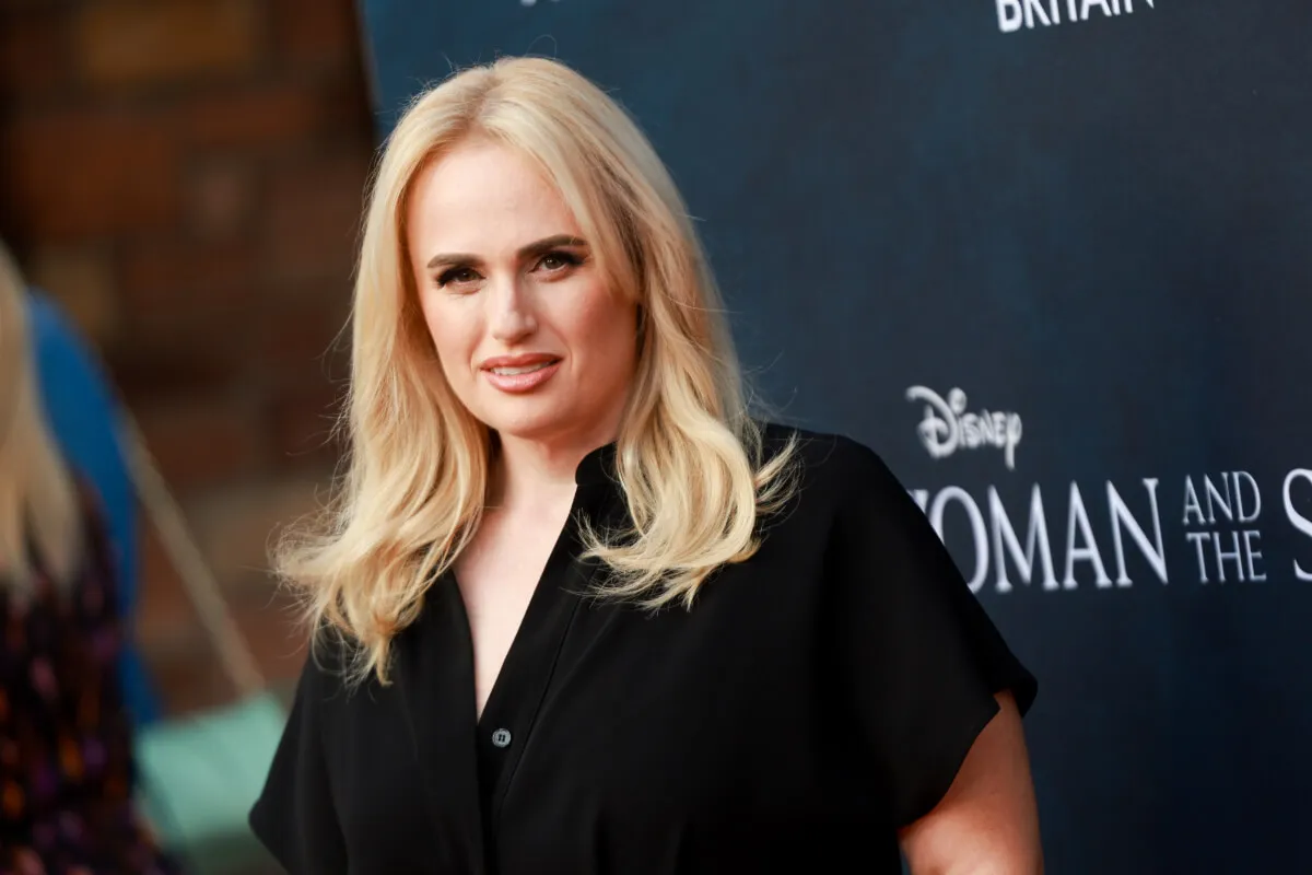 Rebel Wilson wears a black shirt and stands in front of a black background.