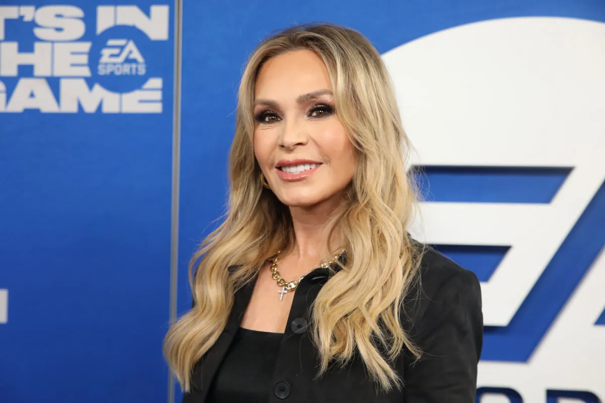 Tamra Judge wears black and stands in front of a blue background.