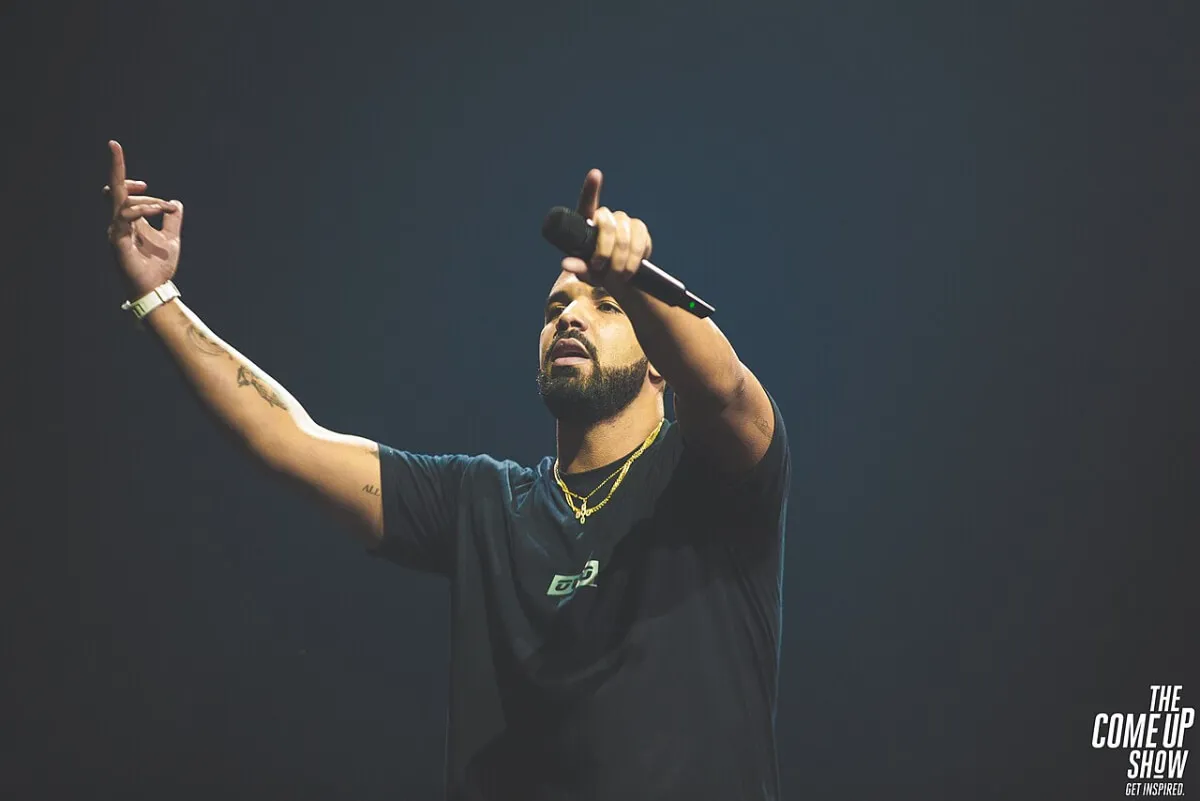 Drake wears a black shirt and holds a microphone.