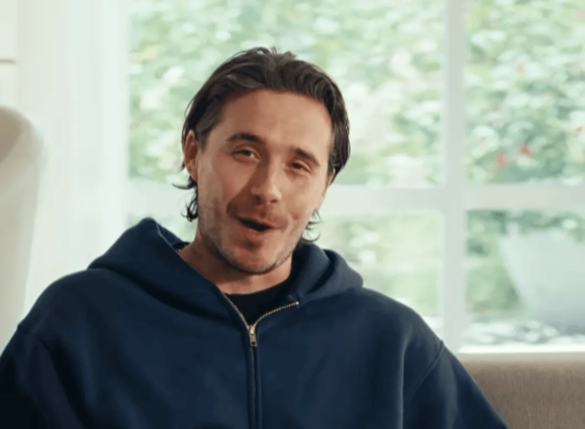 Brooklyn Beckham wears a sweatshirt and sits on a couch in a DoorDash ad.