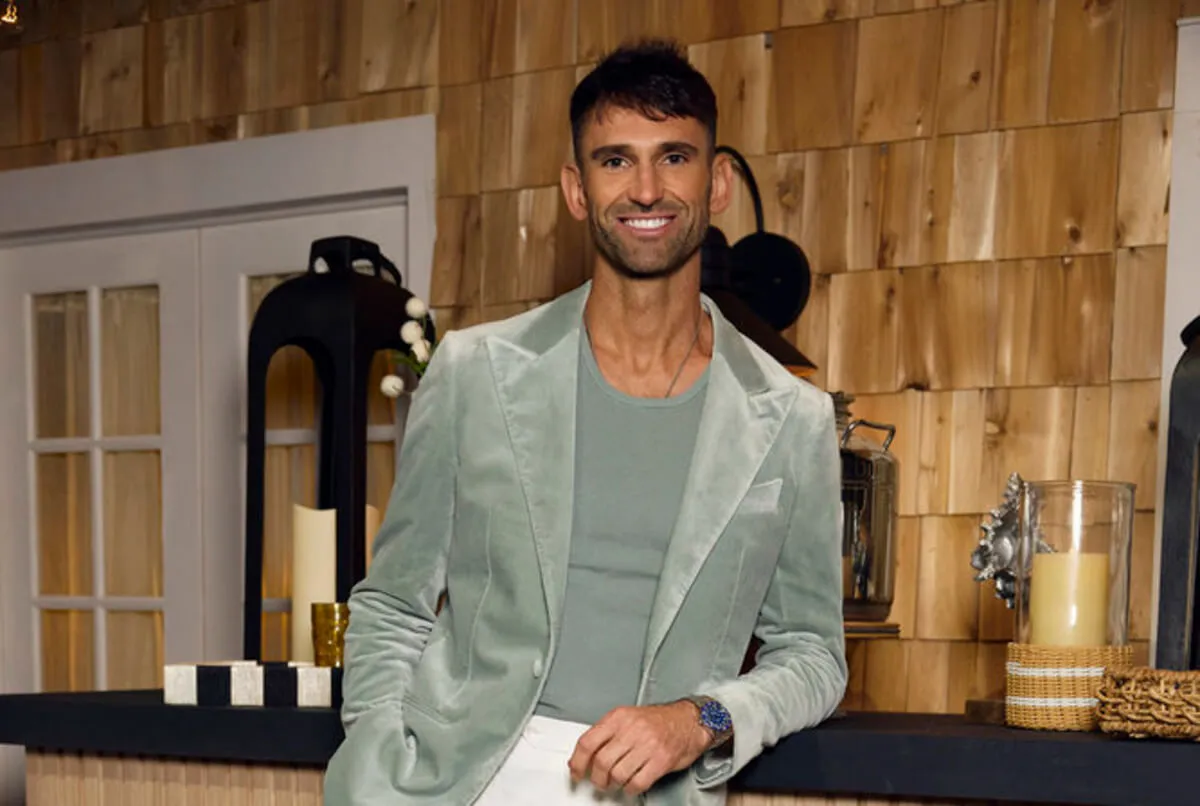 Carl Radke wears a silver blazer and matching shirt. He leans against a bar.