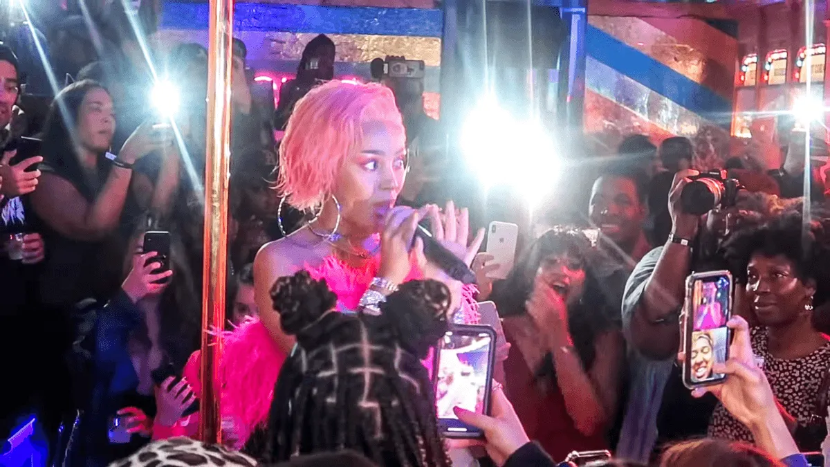 Doja Cat wears a black dress and sings into a microphone.