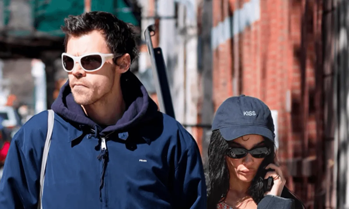 Harry Styles wears sunglasses and a blue jacket while walking with Zoe Kravitz. She wears a baseball hat and sunglasses and talks on the phone.