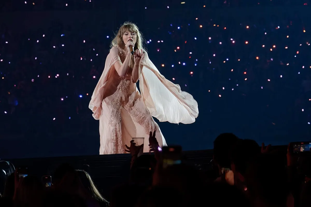 Taylor Swift wears a flowy white dress and sings into a microphone.