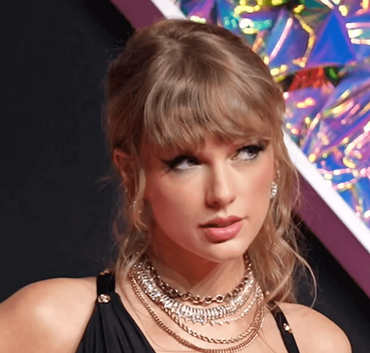 Taylor Swift wears a black dress with gold necklaces.