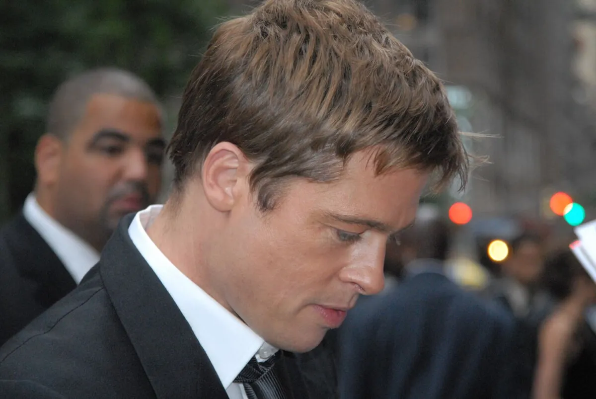 Brad Pitt wears a suit and looks towards the ground. He is in side profile.