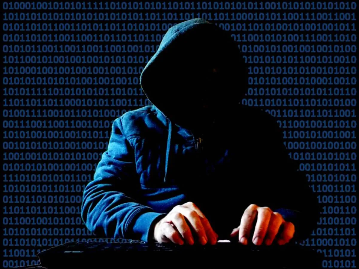 A person in a hoodie with a blank face types on a computer.