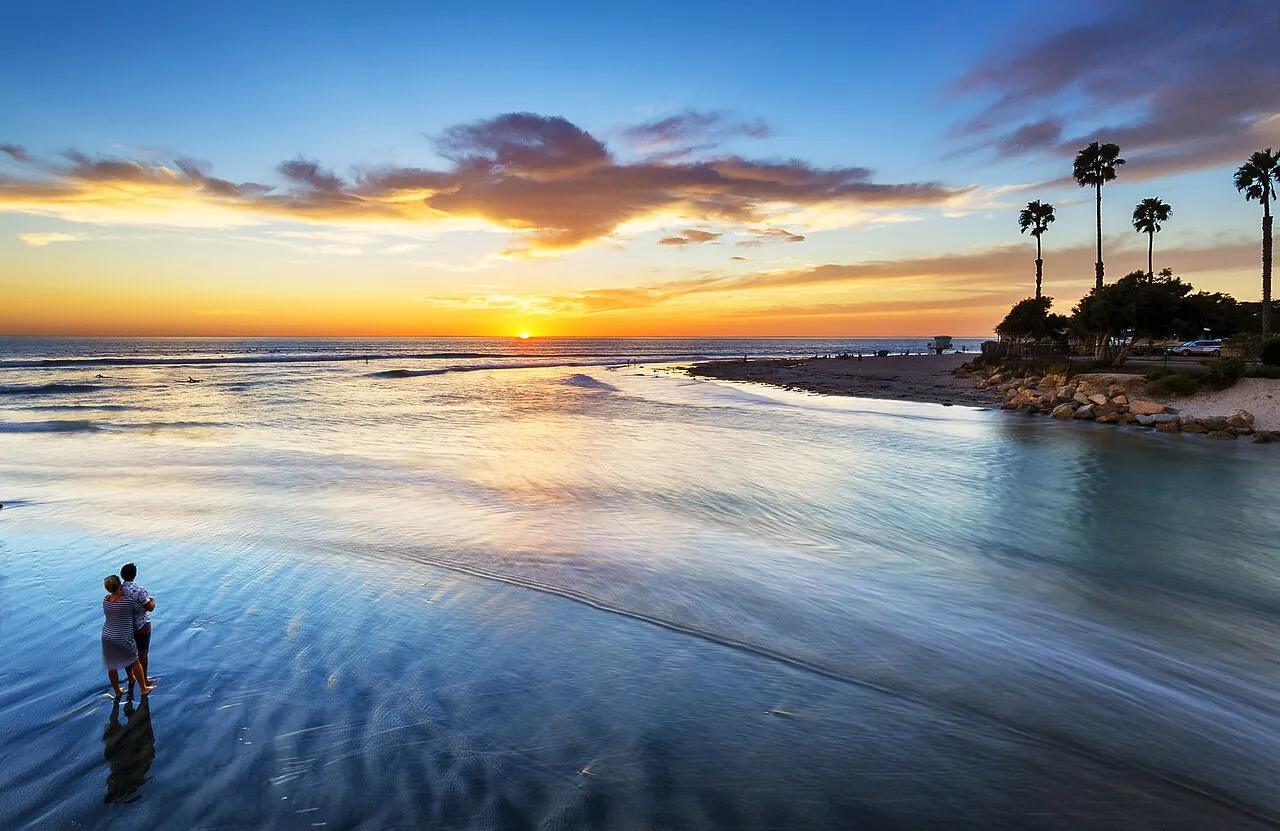 Couple embracing on the beach at sunset with palm trees in the background