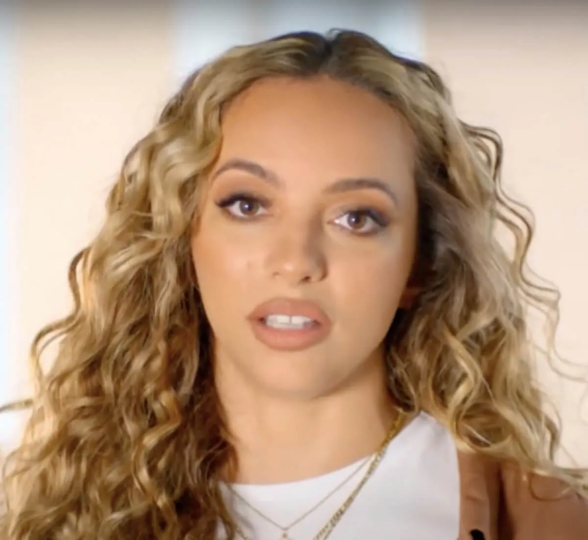 Jade Thirlwall wears a white shirt and brown sweater.