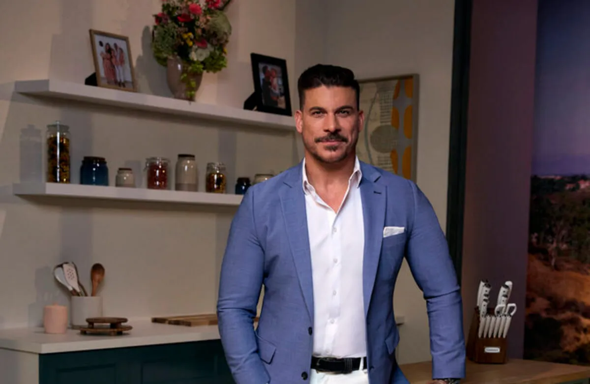 Jax Taylor wears a blue suit jacket and stands in front of a bar.