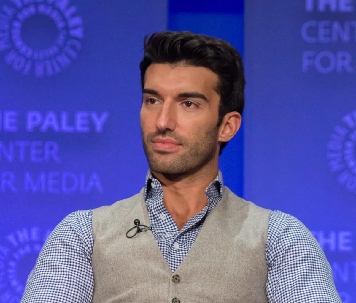 Justin Baldoni wears a blue shirt and gray vest.