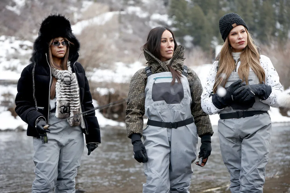 Mary Cosby, Angie Katsanevas, and Britani Bateman wear coveralls and stand in a river.