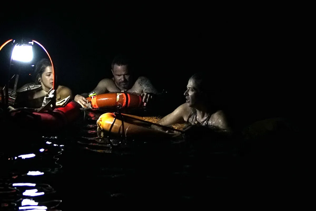Three people clinging to life buoys in dark water in 'Naked and Afraid: Shipwrecked'