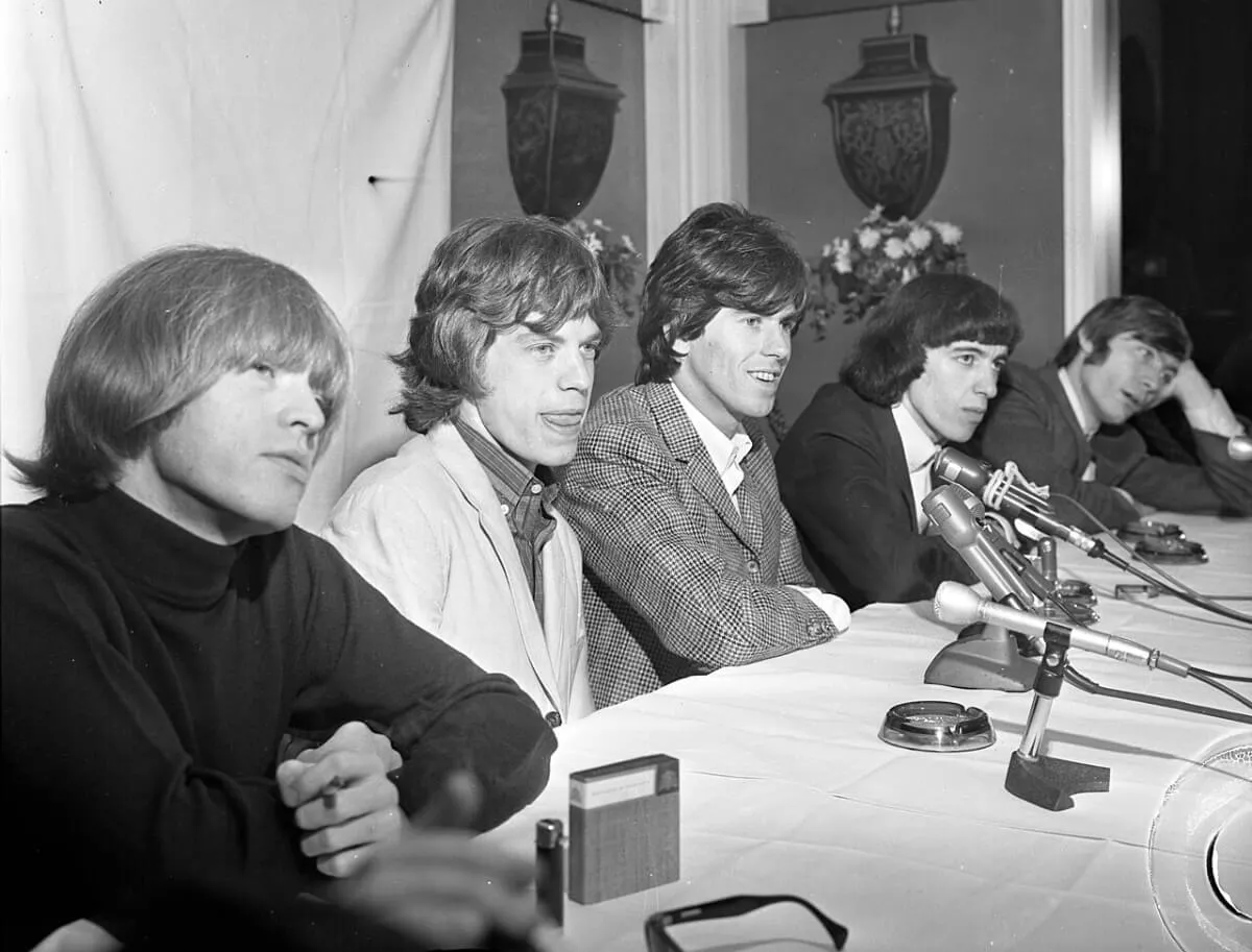A black and white picture of The Rolling Stones sitting at a table.
