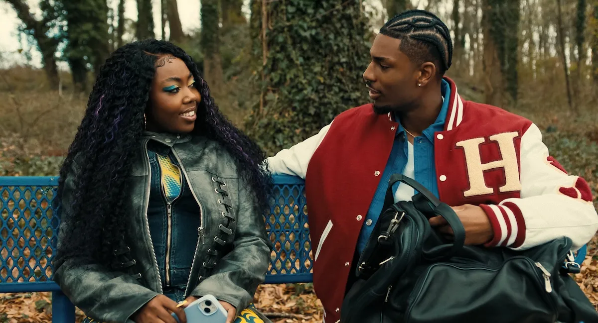 Rashida and Andre sitting next to each other on a bench and smiling in Netflix's 'A Different World'