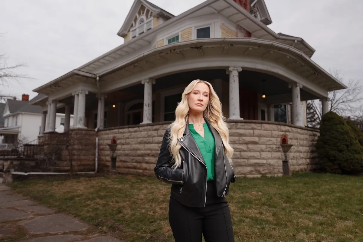 Anna Camp standing in front of a creepy abandoned mansion