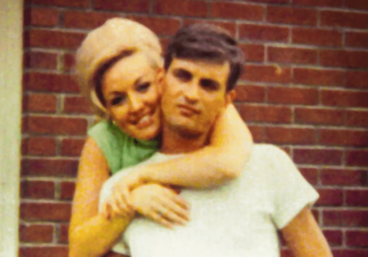 Dolly Parton embraces her husband, Carl Dean, from behind. He wears a white shirt and she wears a green dress.