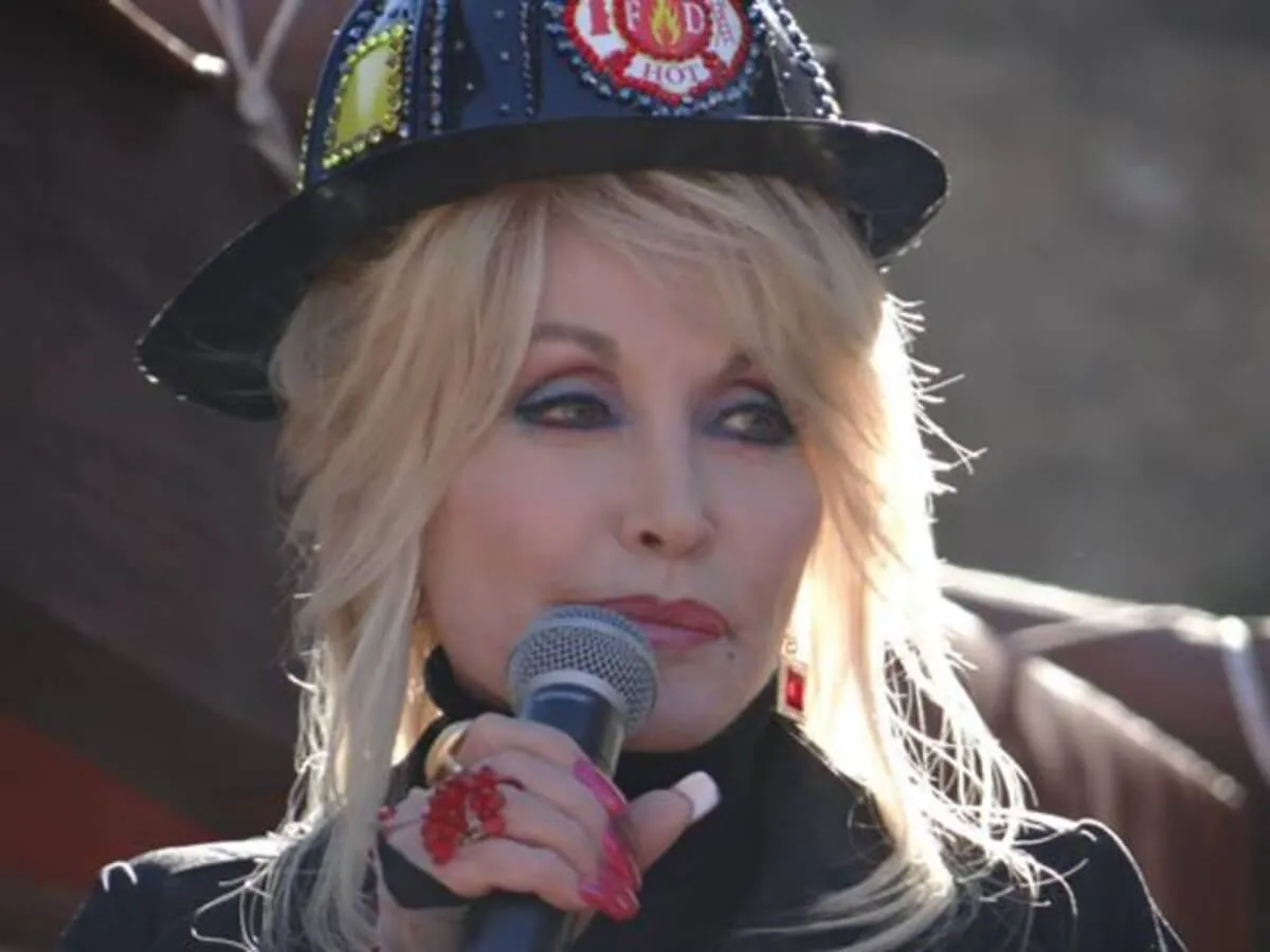 Dolly Parton wears a fire helmet and holds a microphone.