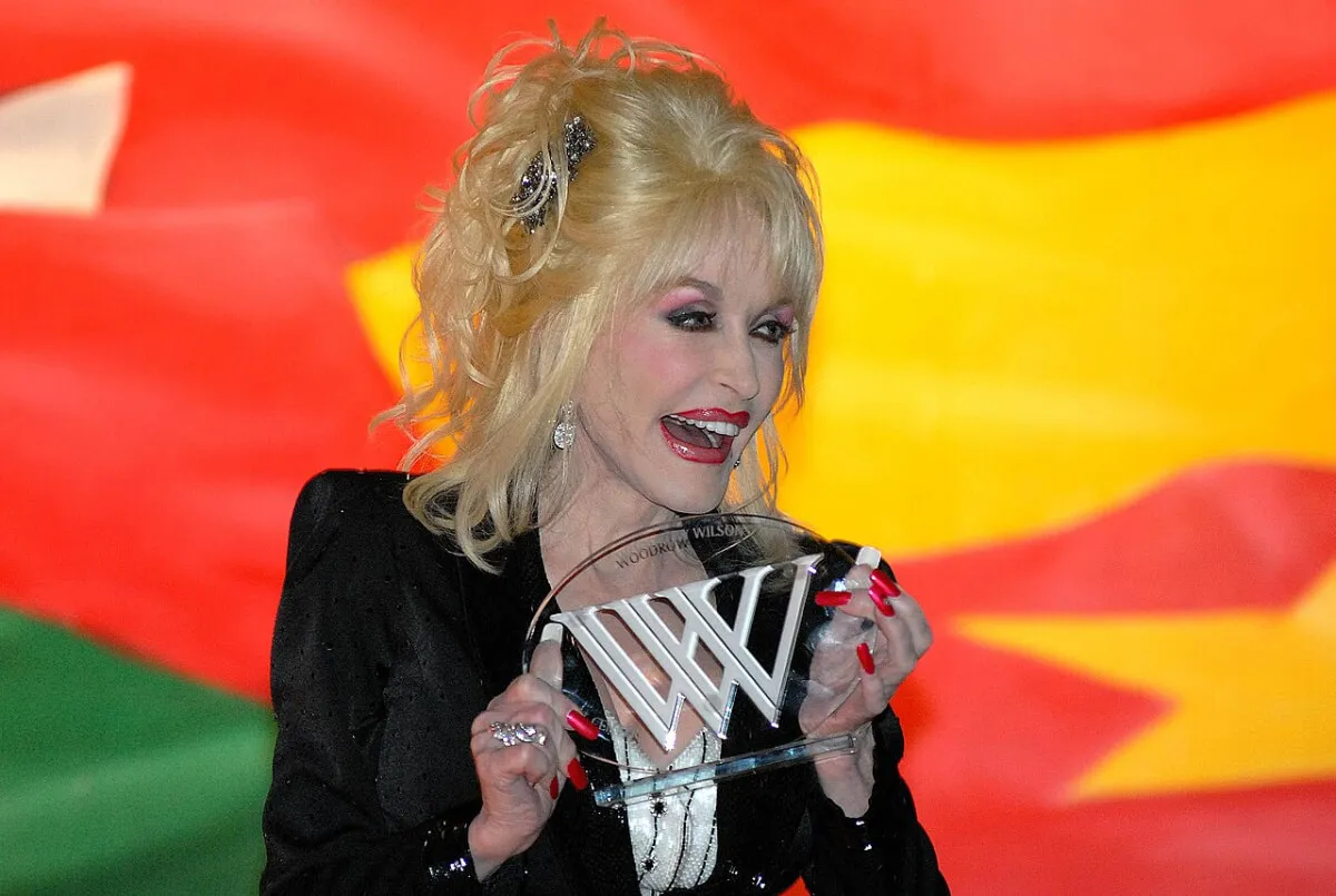 Dolly Parton wears black and holds an award.