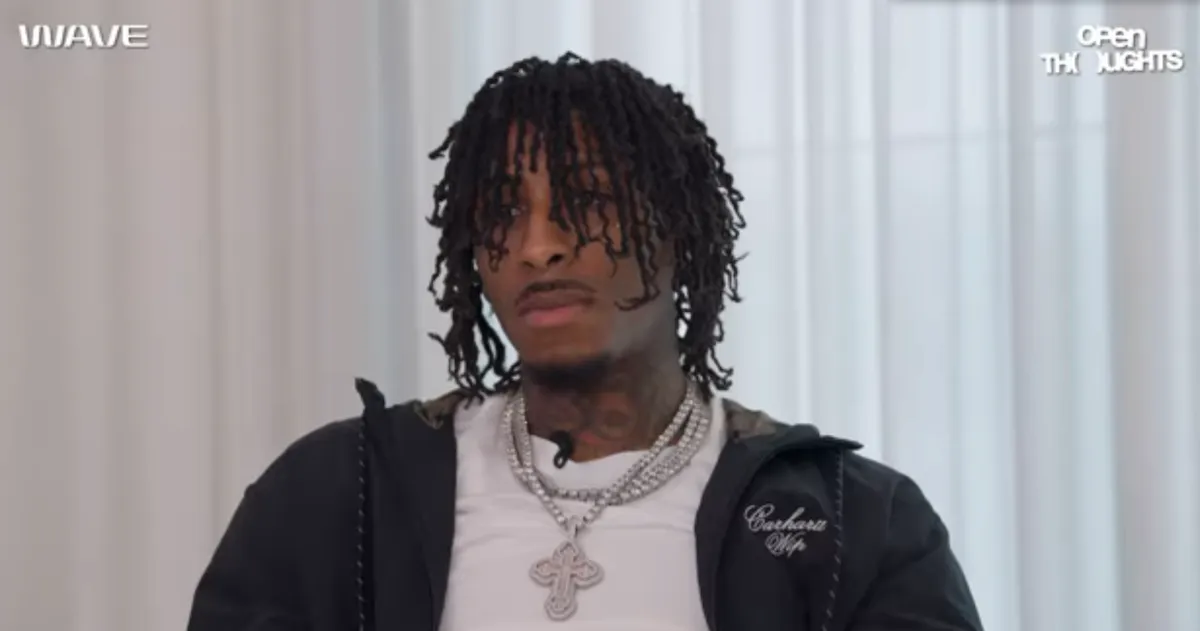 NBA YoungBoy with his hair in his eyes and wearing a large silver cross on a chain