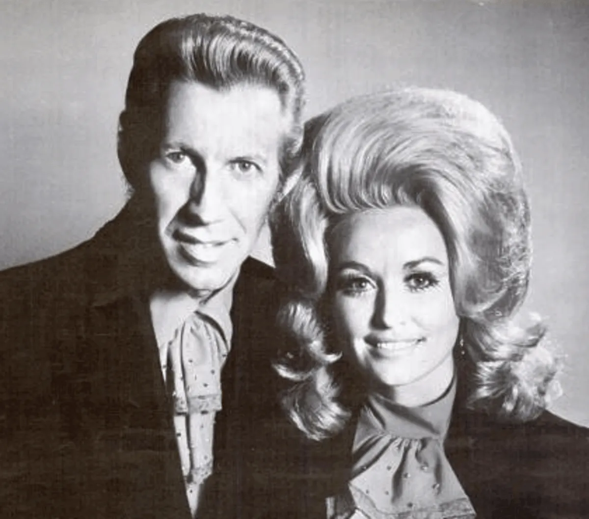 A black and white picture of Porter Wagoner and Dolly Parton smiling.