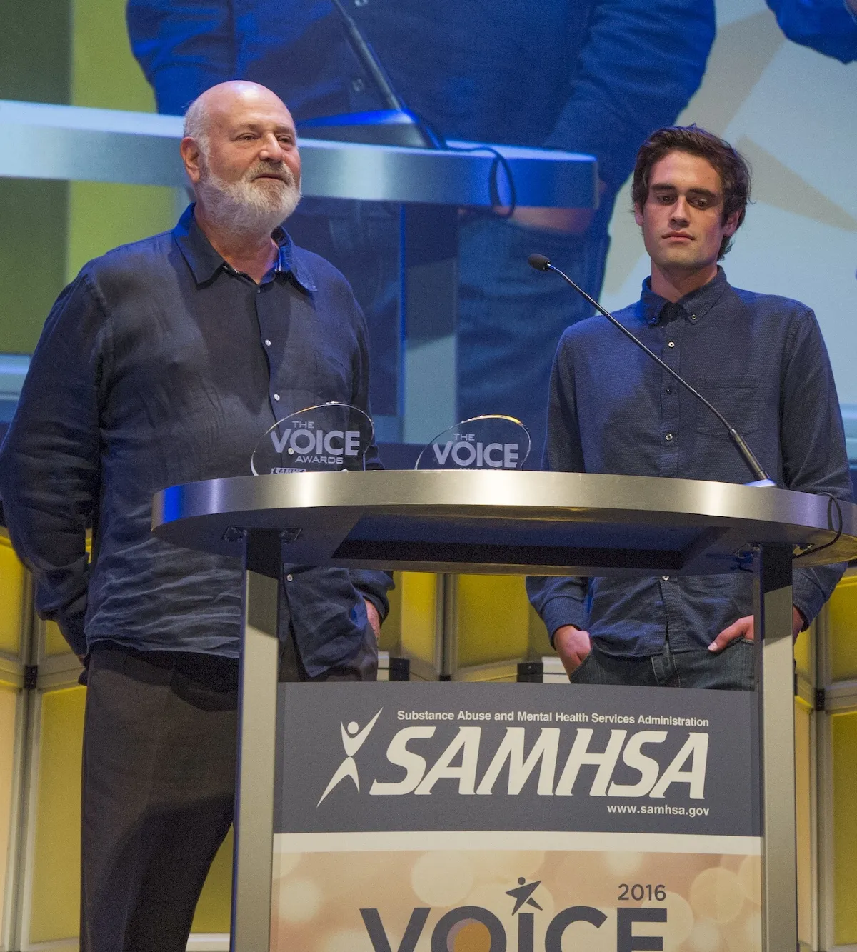 Rob Reiner and Nick Reiner standing behind a lectern at a SAMHSA event