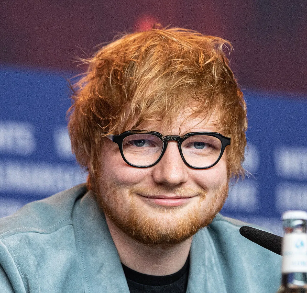Ed Sheeran wears glasses and a blue jacket.